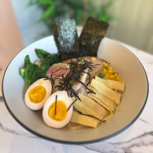 A bowl of Japanese ramen with soft-boiled eggs, bok choy, bamboo shoots, corn, and nori.