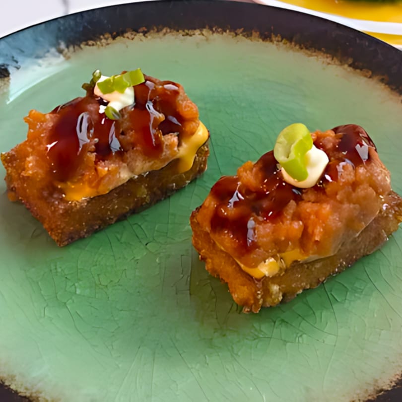 Two pieces of crispy rice sushi topped with spicy tuna, sauce, and green onions on a green plate.