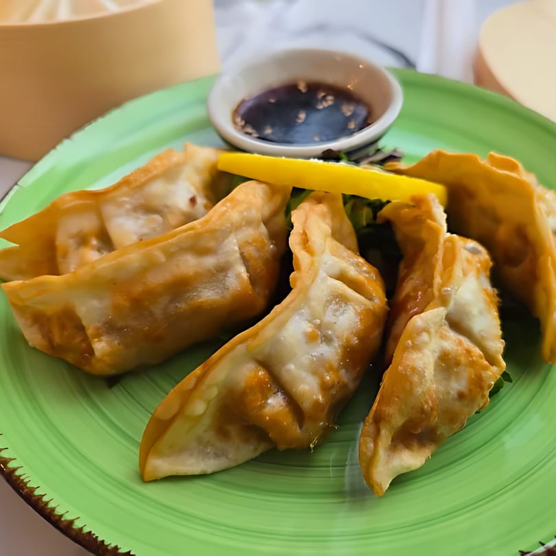 Crispy fried gyoza with a lemon wedge and soy dipping sauce on a vibrant green plate.