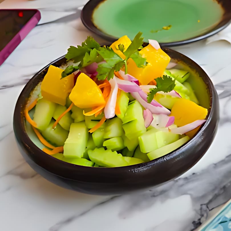 A vibrant Japanese salad with cucumber, mango, red onion, and cilantro in a dark bowl.
